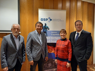 Vier Personen posieren vor einem Banner der Gesellschaft für Sicherheitspolitik (GSP), Sektion Lippstadt.