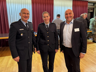 Zwei Offiziere in dunkler Uniform und Detlef W. Karlroth von der GSP im Anzug lächeln bei einer Veranstaltung.