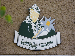 Schild des Gebirgsjägermuseums, das einen Soldaten in Uniform mit einer Edelweißblume zeigt.