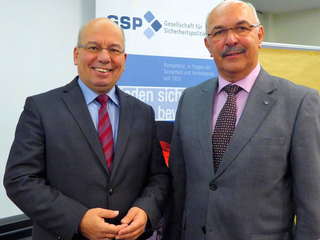 Zwei lächelnde Männer in Anzügen vor einem Banner der Gesellschaft für Sicherheitspolitik (GSP).
