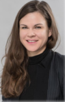Porträt einer lächelnden Frau mit langen braunen Haaren, schwarzem Rollkragenpullover und Nadelstreifenblazer.