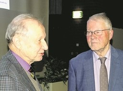 Zwei ältere Herren, einer mit Brille im blauen Anzug, der andere in einem gemusterten Sakko, unterhalten sich.