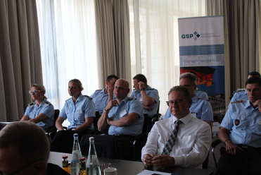 Teilnehmer, viele in hellblauen Uniformen, sitzen bei einer Konferenz oder Tagung; im Hintergrund ein GSP-Banner.