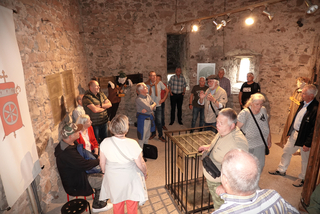 Geführte Tour in einem historischen Steinsaal. Ein Sprecher wendet sich an Besucher inmitten historischer Exponate und Mannequins.