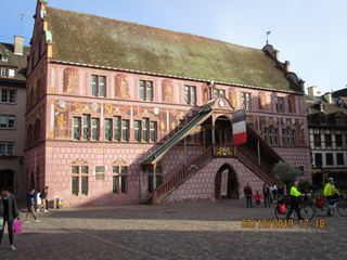 Das historische Koifhus-Gebäude in Colmar, Frankreich, mit rosafarbener Fassade, Wandmalereien und Doppeltreppe.