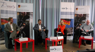 Vier Podiumsteilnehmer bei einer Sicherheitspolitik-Veranstaltung, mit Bannern der GSP und des Reservistenverbands.
