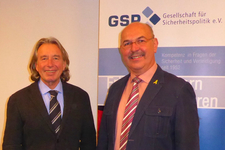 Zwei lächelnde Männer, einer mit langen Haaren, der andere mit Schnurrbart, vor dem GSP-Banner.