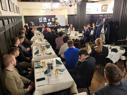 Formelles Abendessen mit einem Redner, der Gäste an langen Tischen anspricht.