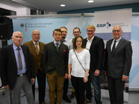 Acht Personen, darunter eine Frau, posieren für ein Gruppenfoto vor Bannern des Bundespresseamtes und der GSP.