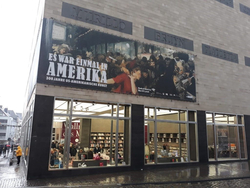 Museumsfassade mit großem Banner für "Es war einmal in Amerika: 300 Jahre US-amerikanische Kunst" über einem belebten Geschäft.