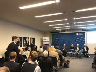 Ein junger Mann mit Mikrofon stellt eine Frage bei einer Podiumsdiskussion der Konrad-Adenauer-Stiftung.