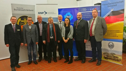 Gruppe von 9 Personen bei einer deutschen Militär- und Politikveranstaltung vor Organisationsbannern.