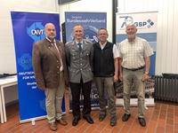 Vier lächelnde Männer, einer in Bundeswehr-Uniform, stehen vor Bannern des BundeswehrVerbandes, DWT und GSP.