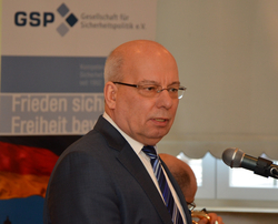 Ein Mann mit Brille, Anzug und gestreifter Krawatte spricht in ein Mikrofon vor einem GSP-Banner.