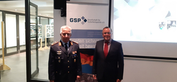 Zwei Männer, einer in Militäruniform, der andere im Anzug, stehen vor einem GSP-Banner und der deutschen Flagge.