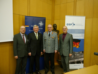 Vier Männer, darunter ein General, stehen vor Bannern der Deutschen Gesellschaft für Sicherheitspolitik und der NATO.