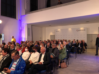 Menschen sitzen in einem Saal bei einer Townhall-Veranstaltung mit 'Zeitenwende on tour'-Branding. Einige tragen Masken.
