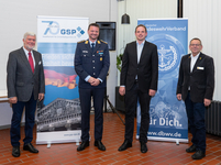 Vier lächelnde Männer, einer in Uniform, stehen vor Bannern der Gesellschaft für Sicherheitspolitik und des BundeswehrVerbands.