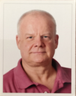 Passfoto eines älteren Mannes mit kurzen hellen Haaren, blauen Augen und einem weinroten Poloshirt.