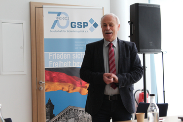 Ein lächelnder Mann vor einem Banner der Gesellschaft für Sicherheitspolitik (GSP), das ihr 70-jähriges Bestehen feiert.