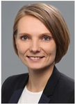 Professionelles Porträt einer lächelnden Frau mit hellbraunem Haar im dunklen Blazer.