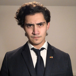 Junger Mann mit dunklem Haar und ernstem Blick, trägt Anzug mit Krawatte und einer deutschen Flaggen-Anstecknadel.