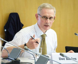 Uwe Backes, ein Mann mit Brille und gemusterter Krawatte, spricht an einem Konferenztisch, einen Stift haltend.