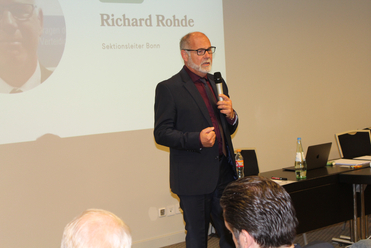 Richard Rohde, Sektionsleiter Bonn, spricht vor Publikum und hält ein Mikrofon.