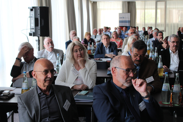 Eine vielfältige Gruppe von Erwachsenen sitzt an Tischen und nimmt aufmerksam an einer Konferenz oder einem Meeting teil.