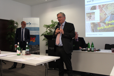 Ein Mann im Anzug spricht in ein Mikrofon während einer Präsentation.