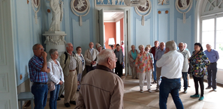Gruppe älterer Personen in einem prunkvollen Raum mit hellblauen Wänden, Statuen und klassischen Stuckverzierungen.
