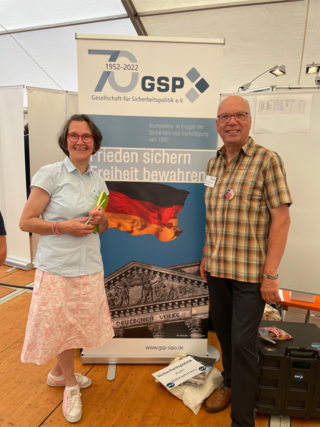 Zwei lächelnde Personen, eine Frau und ein Mann, stehen vor einem Banner der GSP, das ihr 70-jähriges Jubiläum und das Reichstagsgebäude zeigt.