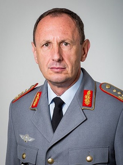 Porträt eines Mannes in grauer Militäruniform mit aufwendigen Schulterstücken und Kragenspiegeln, eine Krawatte tragend.