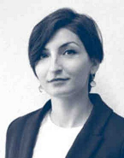 Porträt einer Frau mit kurzen dunklen Haaren, die eine dunkle Jacke über einem weißen Oberteil trägt und lächelt.