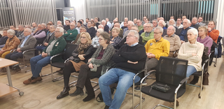 Zahlreiche Personen, überwiegend ältere Erwachsene, sitzen als Publikum bei einer Veranstaltung.