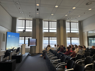 Zuhörer bei einer UN Bonn Präsentation zum Thema "Shaping a Sustainable Future" in einem modernen Konferenzraum mit Stadtblick.