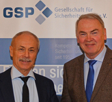 Zwei lächelnde Männer in Businesskleidung vor einem Hintergrund mit dem "GSP Gesellschaft für Sicherheit"-Logo.