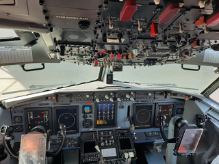 Das komplexe Cockpit eines Flugzeugs, mit zahlreichen Bildschirmen, Anzeigen, Schaltern und Hebeln auf der Instrumententafel und Überkopf.