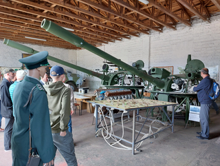 Militärmuseum-Interieur: große grüne Kanonen, uniformierte Schaufensterpuppe, Besucher und ein detailliertes Schlachtfeldmodell.