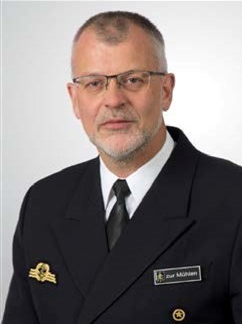 Portrait eines Mannes in dunkler Marineuniform mit Brille und kurzem Bart, ein Namensschild zeigt 'zur Mühlen'.