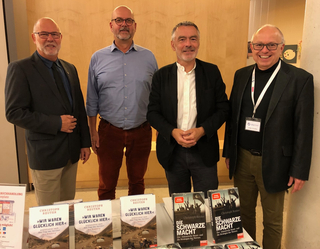 Vier Männer, darunter Autor Christoph Reuter, stehen bei einer Veranstaltung hinter einem Tisch mit seinen Büchern.