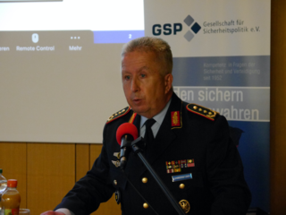 Oberst Habersetzer in Uniform spricht vor einem Mikrofon bei einer Veranstaltung der Gesellschaft für Sicherheitspolitik (GSP).