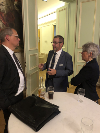 Drei Fachleute unterhalten sich bei einem Empfang, an einem Tisch mit Getränken stehend.