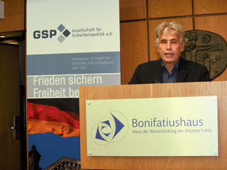 Mann spricht am Rednerpult mit GSP- und Bonifatiushaus-Schildern im Hintergrund.