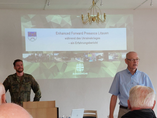 Ein Soldat und ein älterer Mann präsentieren über Enhanced Forward Presence in Litauen während des Ukrainekrieges, mit Bundeswehr-Logo.