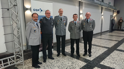 Fünf Männer in Uniformen, wahrscheinlich Militäruniformen, posieren vor einem Banner der Gesellschaft für Sicherheitspolitik (GSP).