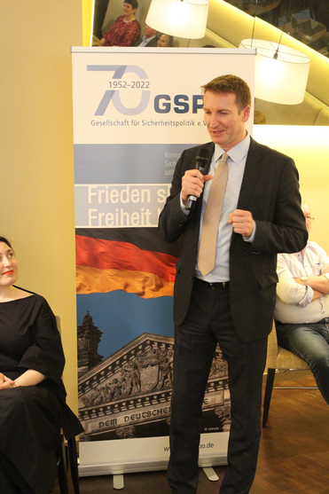 Mann im Anzug spricht auf einer GSP-Veranstaltung, mit Banner zur '70 Jahre 1952-2022 Gesellschaft für Sicherheitspolitik'.