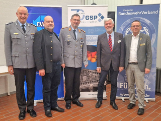 Fünf Männer, darunter zwei in Militäruniformen, lächeln vor Bannern deutscher sicherheitspolitischer Verbände.