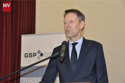 Mann im Anzug spricht an einem Rednerpult vor einem Banner mit dem GSP-Logo im Hintergrund.