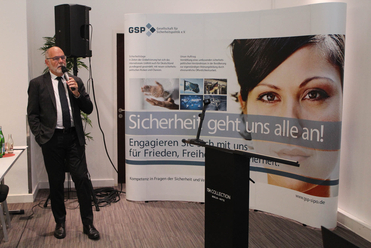 Mann spricht auf GSP-Veranstaltung vor Banner 'Sicherheit geht uns alle an!'. Gesellschaft für Sicherheitspolitik e.V.